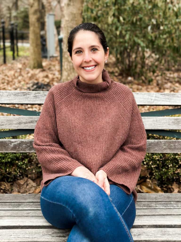A photo of a warm, smiling therapist Paige Scrofani sitting on a bench outdoors in New York City
